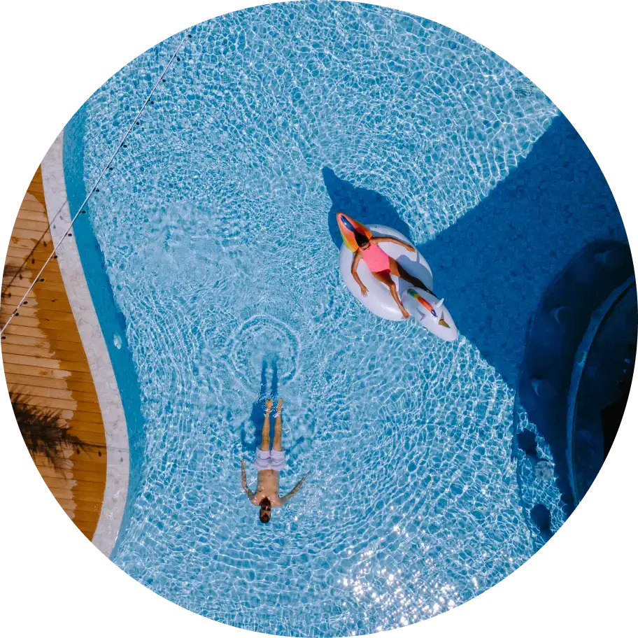 Aerial view of a clear blue pool. One person floats calmly on their back. Another lounges on a unicorn float.
